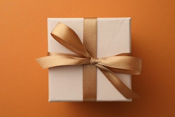 Poster - Beautiful gift box with golden bow on orange background, top view