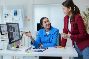 Two smiling businesswomen discussing charts and data displayed on computer in a bright modern office