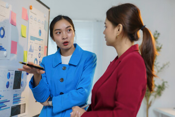 Two businesswomen are having a meeting in the office, discussing charts and graphs on a whiteboard