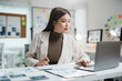 ©  NCST Studio - Young asian businesswoman analyzing charts and working with laptop computer at her desk in modern office