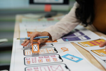Designer is holding a paper prototype interface for a mobile phone app, developing a new product