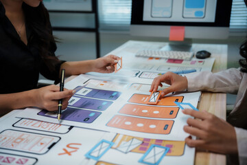 two ux designers are discussing user experience of mobile application prototype on a table with pape