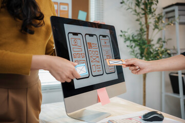 two female user experience designers are comparing paper prototypes of a mobile application interfac