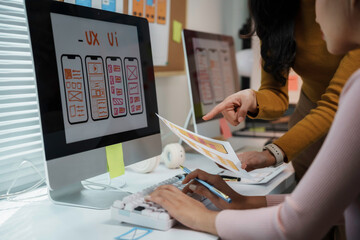 Two web designers are discussing a new mobile application interface displayed on a computer screen