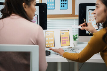 Two female uiux designers are discussing the user interface of a mobile application in their office