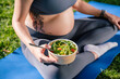 © zinkevych - Pregnant woman holding plate with salad eating after yoga exercising sitting on green grass