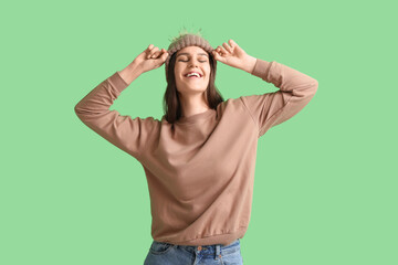 Wall Mural - Happy young woman in winter clothes on green background