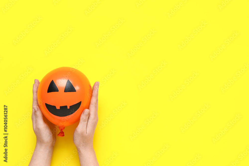 Female hands with funny Halloween orange balloon on yellow background