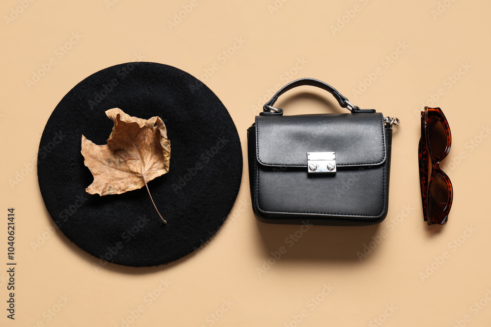 Stylish bag, hat, sunglasses and dry leaf on beige background