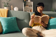 © Zamrznuti tonovi - Asian woman reading book while relaxing on a green comfortable sofa.