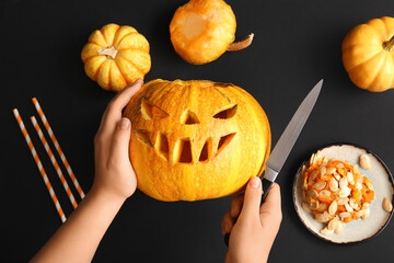 Sticker - Female hands with carved Halloween pumpkins, plate of seeds and knife on black background