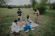 © qunica.com - A diverse group of friends and colleagues socialize over a picnic in a lush park. They engage in conversation and enjoy food, surrounded by greenery and nature's tranquility.