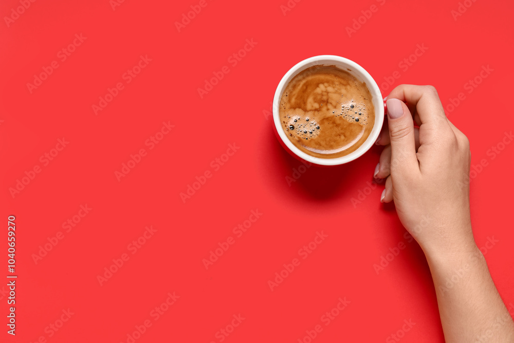 Female hand with cup of coffee on red background