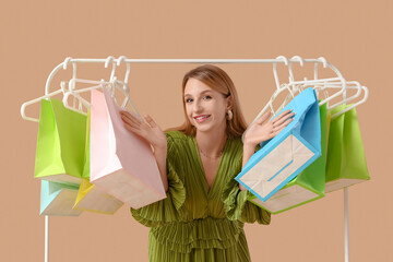 Wall Mural - Beautiful young happy woman with shopping bags on rack against beige background