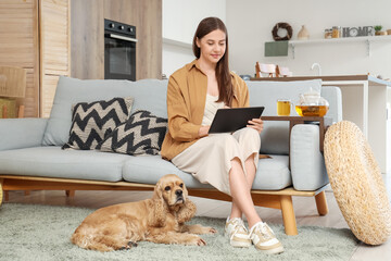 Poster - Beautiful young happy woman and cute Cocker Spaniel dog with cup of green tea sitting on sofa at home