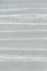 Wave patterns in white beach sand with horizontal stripes, photo taken at close-up macro. A graphic resource, creative design, surfaces, and backgrounds. Vertical.
