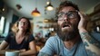 © Dulemegapixel - A tattooed man and a woman react with surprise and intense emotions at a cafe, highlighting unexpected situations and spontaneous emotional responses in daily life.