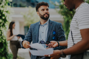 Multicultural team members in an outdoor city meeting brainstorm ideas and strategies for business growth. Engaged in discussion, holding documents, and creating plans for future success.