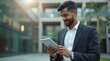 © NASSRI - Focused successful mature Indian or Latin entrepreneur businessman holding digital pc tablet standing outdoor at business office building. Hispanic smiling man in suit working using touchpad computer