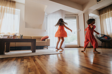 Wall Mural - Two children joyfully spin and dance in a sunlit living room, expressing happiness and freedom. The interior features a cozy couch and wooden floors.