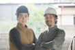 © kapinon - Two people wearing helmets working in work gattens in work clothes, smiling for the camera.