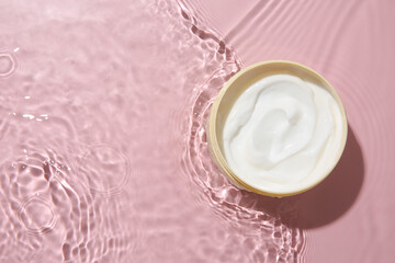 Wall Mural - Cosmetic product. Jar with cream in water on pink background, top view. Space for text