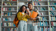 © Yuliia - Two students classmates African American man Indian Latino Arabian woman mobile phone smartphone library smile pleasure laugh communication internet web girl guy education university learning study