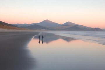 Two people walking on a beach with mountains in the background