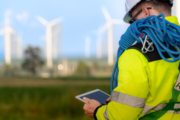 two engineers in high visibility jackets and helmets are inspecting a wind farm. one is holding a mo