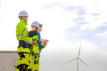 two engineers wearing high visibility safety jackets and helmets measure wind speed with an anemomet