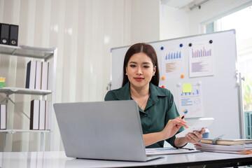 Young Accountant Analyzing Financial Documents on Laptop in Modern Office Setting with Charts and Graphs in Background