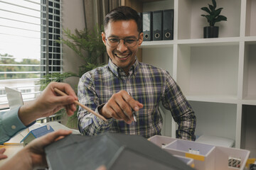 A team of engineers meets in the office to analyze the design structure to ensure it meets the client's wants. A team of architects and contractors meets to discuss the design based on a model house.