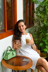 Portrait of 39 years old russian woman without make up sitting with glass of ice coffee in white dress