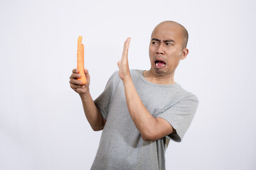 Indonesian bald man looks disgusted and disgusted while holding some carrots
