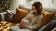 © Berkah - Young pregnant woman sitting on couch in living room.