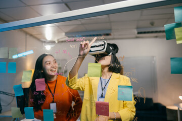 Two businesswomen brainstorming and planning a project using virtual reality technology and writing notes on a glass wall in the office