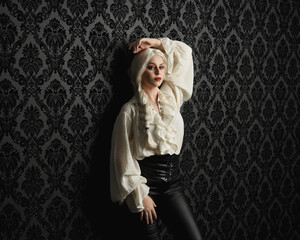 Canvas Print - close up portrait of beautiful blonde female model, wearing vintage gothic fantasy ruffle blouse white shirt, leather pants and long blonde plaited hair.  moody black brocade wall paper background