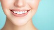 © Phirakhup - Close-up of a smiling woman with healthy teeth against a light blue background.