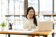 © Nittaya - Confident Businesswoman on a Productive Call:  Smiling businesswoman in a modern office, using laptop and phone, showcasing efficiency and success.