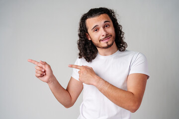 Young man in a white t-shirt and jeans pointing confidently while smiling in a studio setting