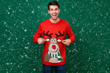 Portrait of attractive cheerful funky brunette guy wearing demonstrating funny jumper isolated over green color background