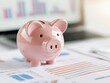 © ParinApril - A cute pink piggy bank on financial documents with graphs and charts in the background, representing savings.
