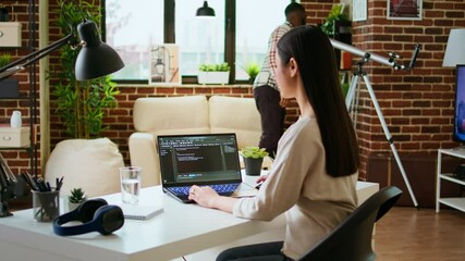 Asian freelancer woman works on programming code in a modern office at home, using her laptop for computer science. IT specialist supports coding, web development and digital innovation. Camera A.