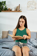 © LIGHTFIELD STUDIOS - A young brunette woman with short stature relaxes on her bed, deeply engaged in a book, surrounded by a cozy and inviting home atmosphere.