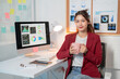 © Tj - Young professional enjoys a cup of coffee while working at her desk. Her computer displays charts and graphs relevant to her work