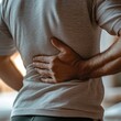© Tadeusz - Man experiencing back pain, showing discomfort while standing in a casual setting.