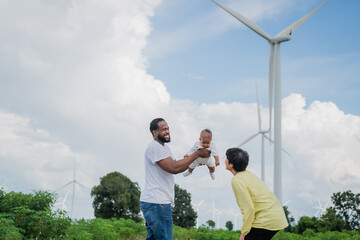 A man and a woman are holding a baby while standing in a field. The baby is flying in the air. The scene has a warm. electrical, engineer, environment, energy, clean, sustainable, wind turbine, nature