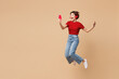 © ViDi Studio - Full body young happy cool woman she wear red t-shirt casual clothes jump high hold in hand use mobile cell phone listen to music in headphones isolated on plain beige background. Lifestyle concept.
