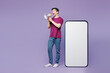 © ViDi Studio - Full body young man he wearing violet t-shirt casual clothes big huge blank screen mobile cell phone smartphone with workspace copy space area scream in megaphone isolated on plain purple background.