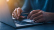 © NaphakStudio - person holding credit card while using laptop, symbolizing online shopping and digital transactions. scene conveys sense of convenience and modern technology.